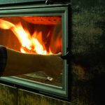 A man's hand is on the glass door of a fireplace