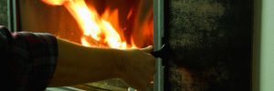 A man's hand is on the glass door of a fireplace